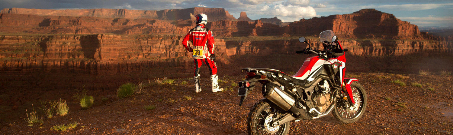 A 2020 red Honda® CRF250L parked next to the canyon's edge with the rider gazing off into the distance